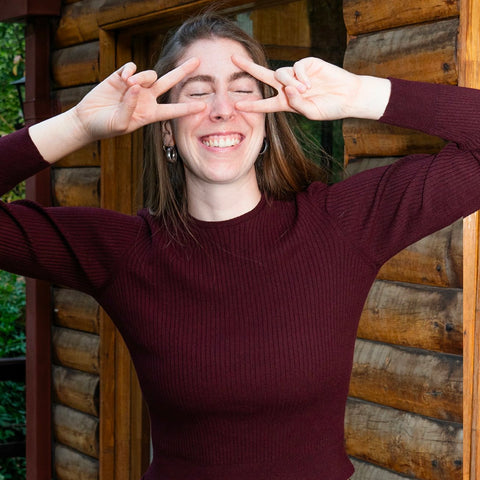 Woman wearing the Cate ribbed top  in maroon making a peace sign