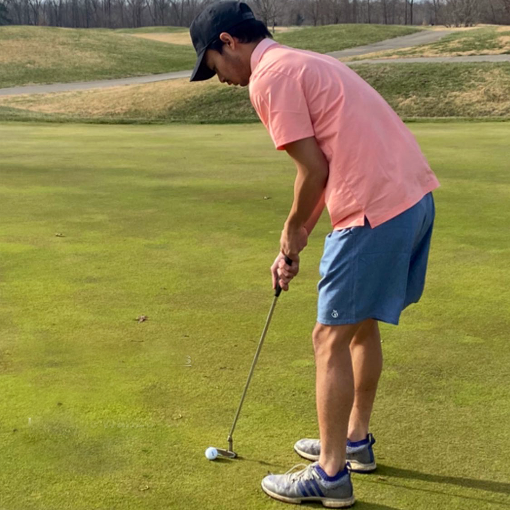 Man putting at a golf course in a pink polo and blue shorts.