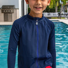 A child in a blue long sleeve rash guard standing in front of a swimming pool