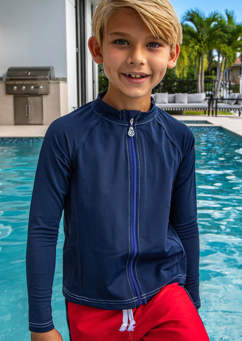 A child in a blue long sleeve rash guard standing in front of a swimming pool