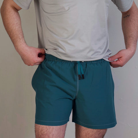 Closeup of the front of a man from the chest down wearing a gray polo and green shorts