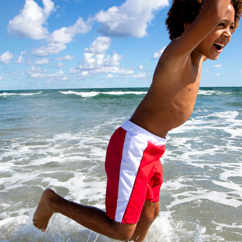 Action shot of a boy jumping into the ocean wearing durable red and white swim trunks