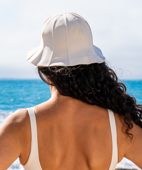 Back of a woman wearing a hat and bikini top in front of the ocean