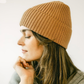 Woman wearing a brown knit beanie against a plain background
