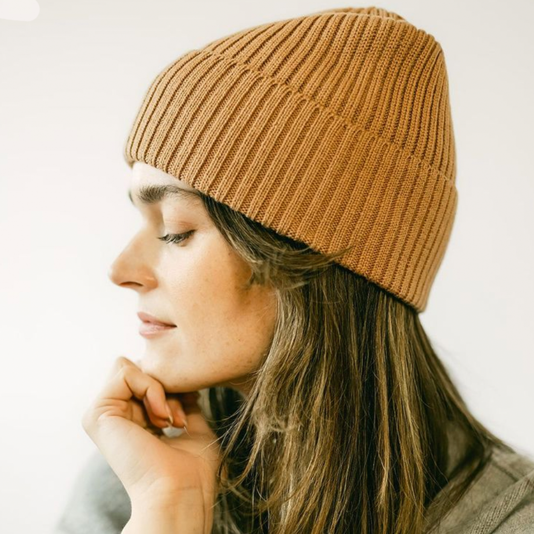 Woman wearing a brown knit beanie against a plain background