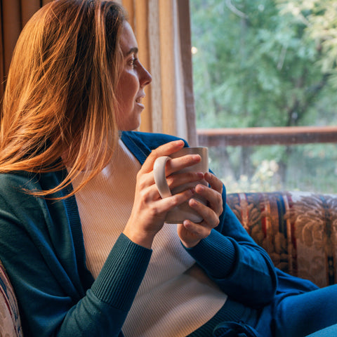 A female model relaxing on a sofa drinking coffee while wearing the Women's Callie Long Sleeve Front Tie Sweater