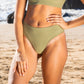 Waist down pic of a woman in a sage green bikini at the beach environmental fashion