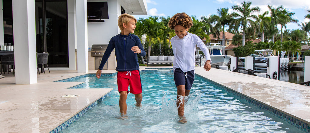 Two boys in swim trunks and rash guards running in a pool