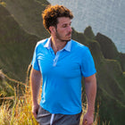 Man on the side of a moutain with the ocean behind him in a blue polo