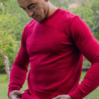 Lifestyle image of a man pulling down the hem of the red crew neck sweater