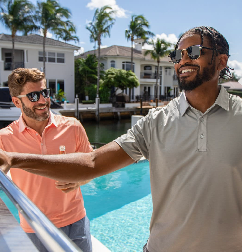 Two men standing by a pool with palm trees and houses in the background