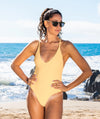 Woman standing in front of the ocean wearing a one piece gold bathing suit