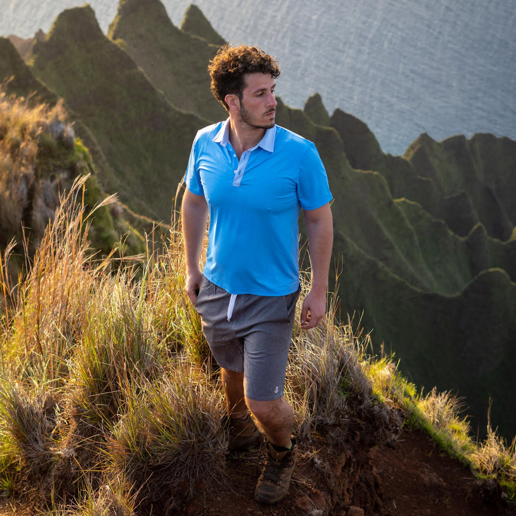 Model wearing Men's Haven Regular Fit 8" Inseam Swim Trunks and NoNetz Cooling Polo standing on a hill with ocean view