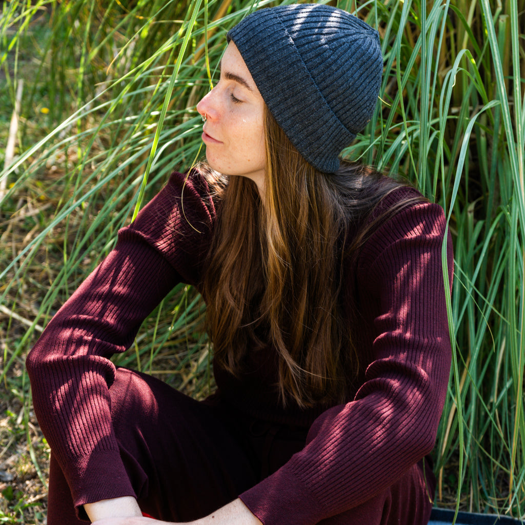 Woman sitting in the grass with a maroon sweat suit and gray beanie