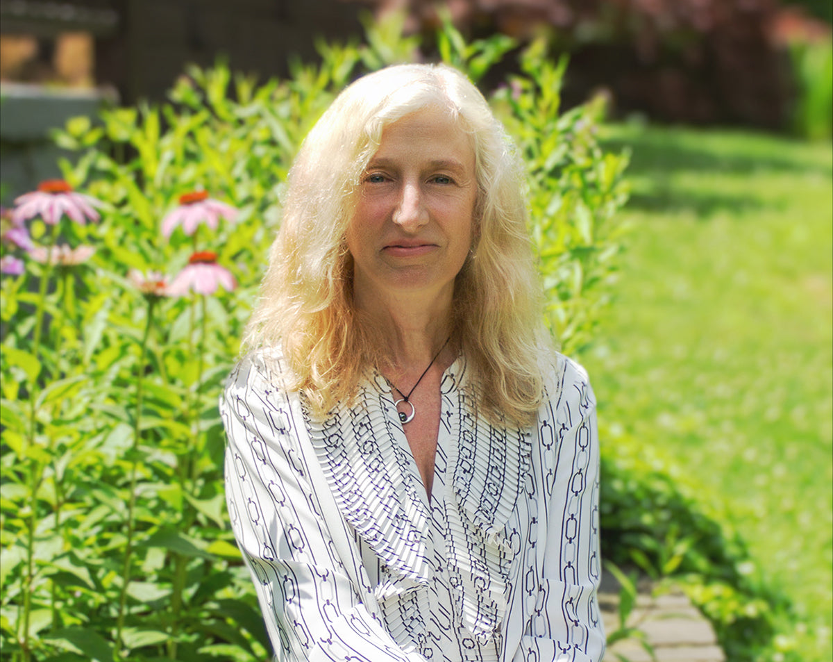 Woman with blonde hair standing in a garden with greenery and flowers.