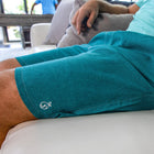 Model lounging on a couch in the teal Haven Regular Fit Swim Trunks