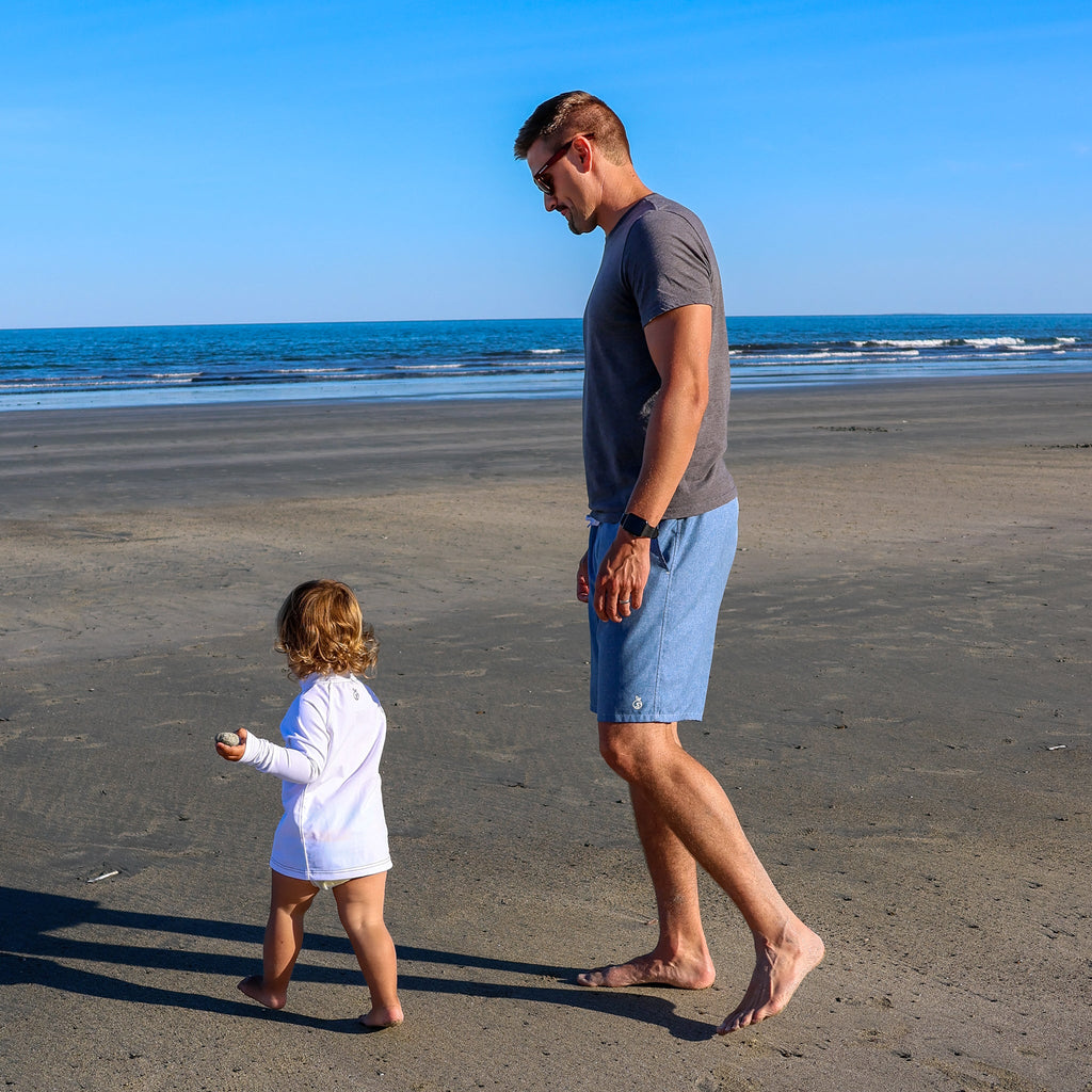 Man and a child strolling on the beach, man is wearing Men's Haven Regular Fit 8" Inseam Swim Trunks. Child is wearing NoNetz White Rashguard